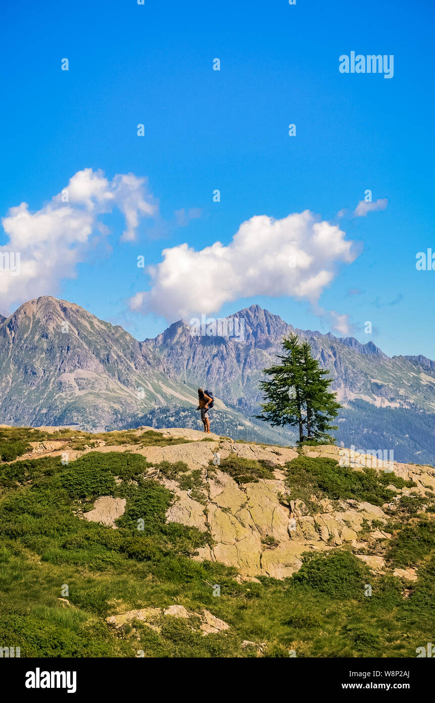 Vertical photo of lone man wandering in mountains on a beautiful sunny day. Standing on the edge of a rock. Backpacking traveler. Active life concept. Stock Photo