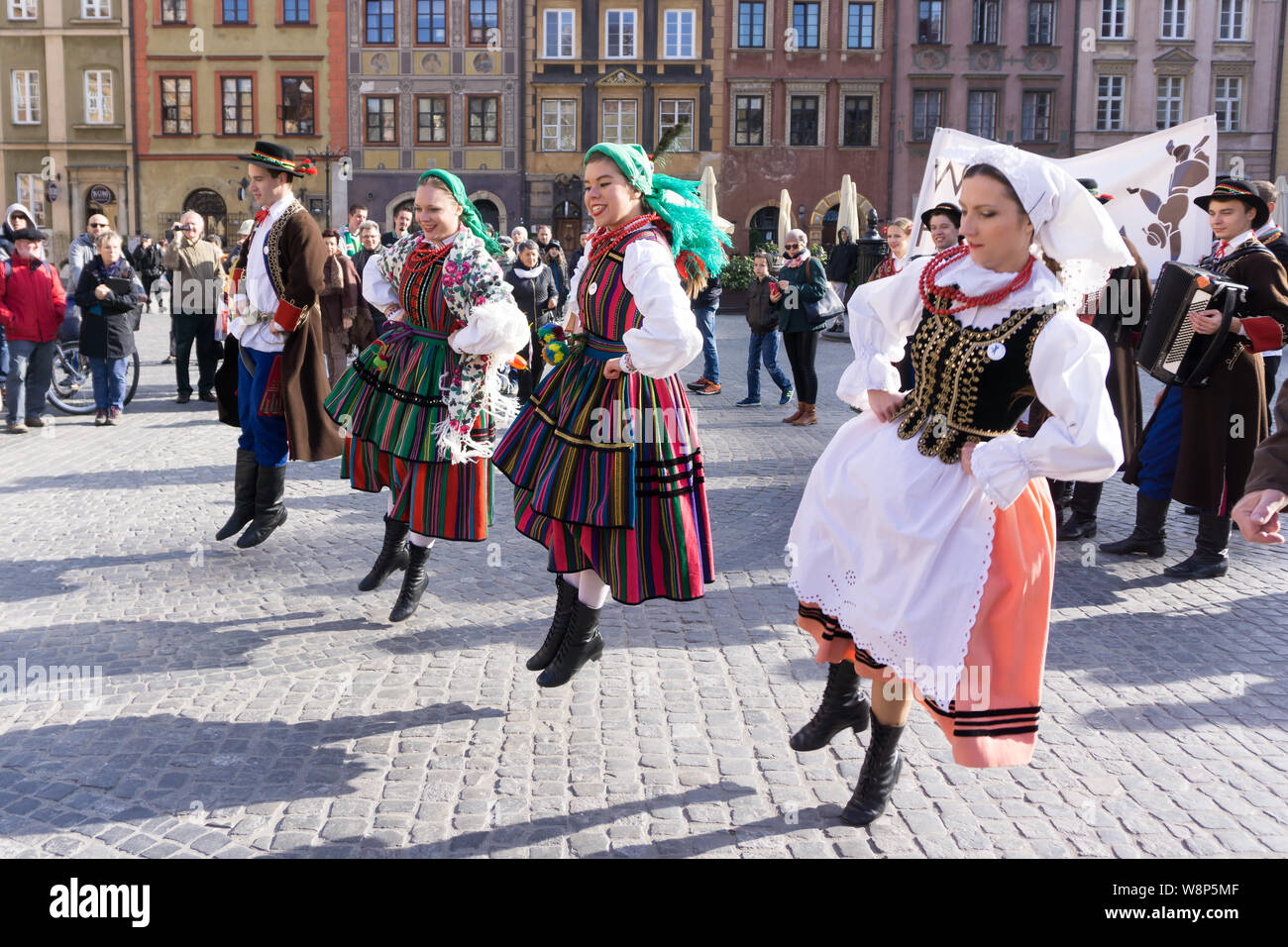 Young people in traditional Lowicz costume are dancing on Warsaw Old Town Square. Dancers dressed in Polish folk costume. Stock Photo