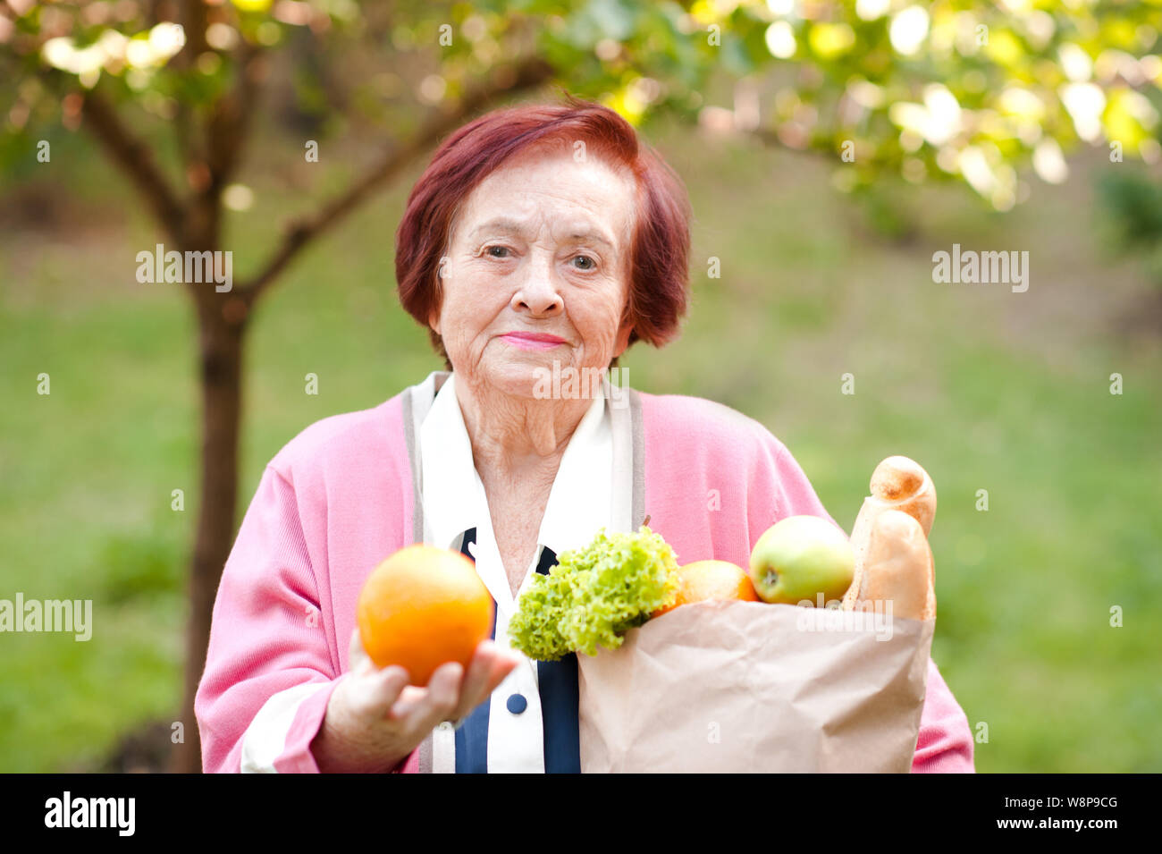 Smiling senior woman 70-75 holding bag with food outdoors closeup. Looking at camera. 80s. Stock Photo