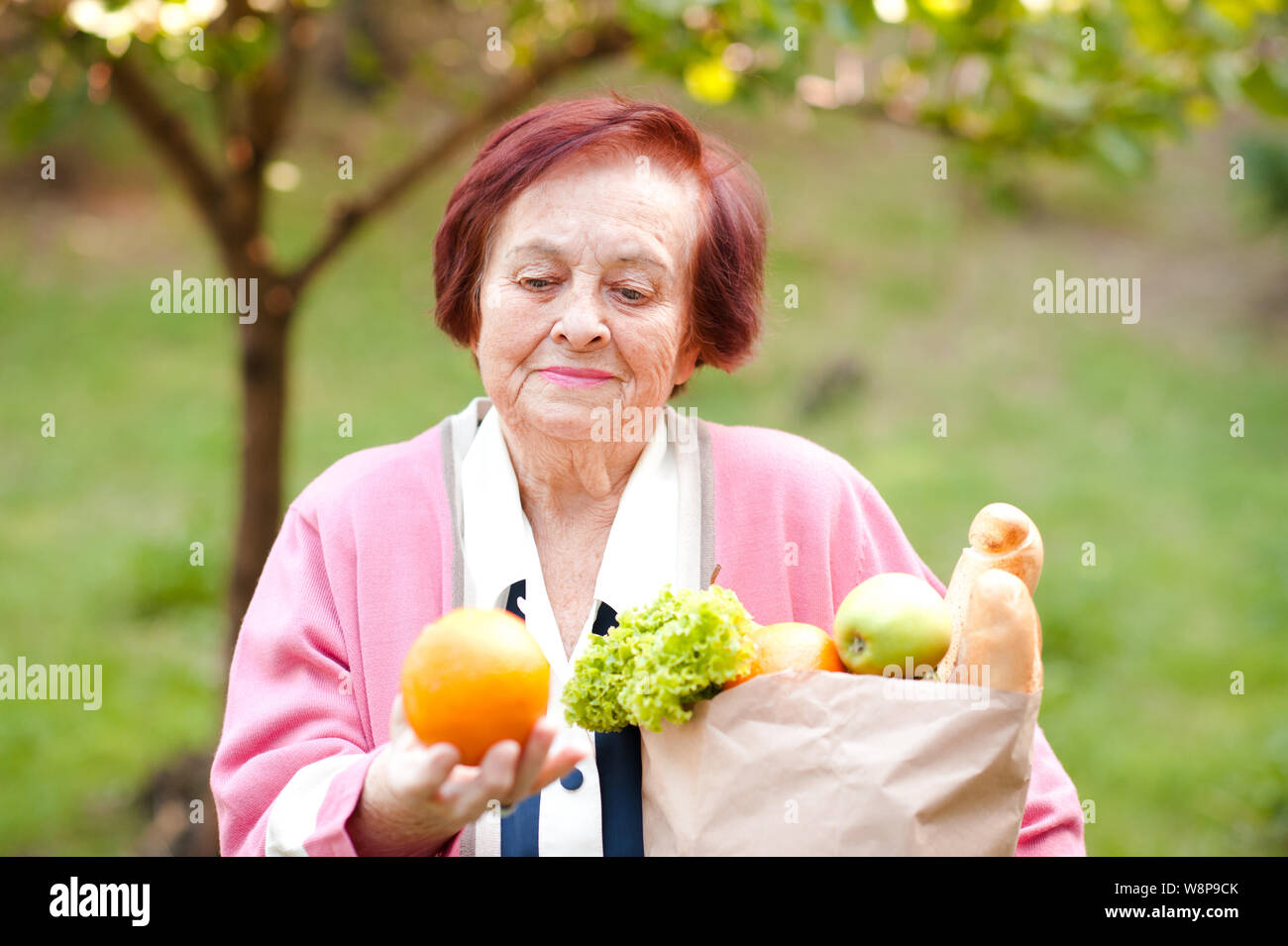 Happy senior woman 70-75 year old holding paper bag with food outdoors close up. 80s. Stock Photo
