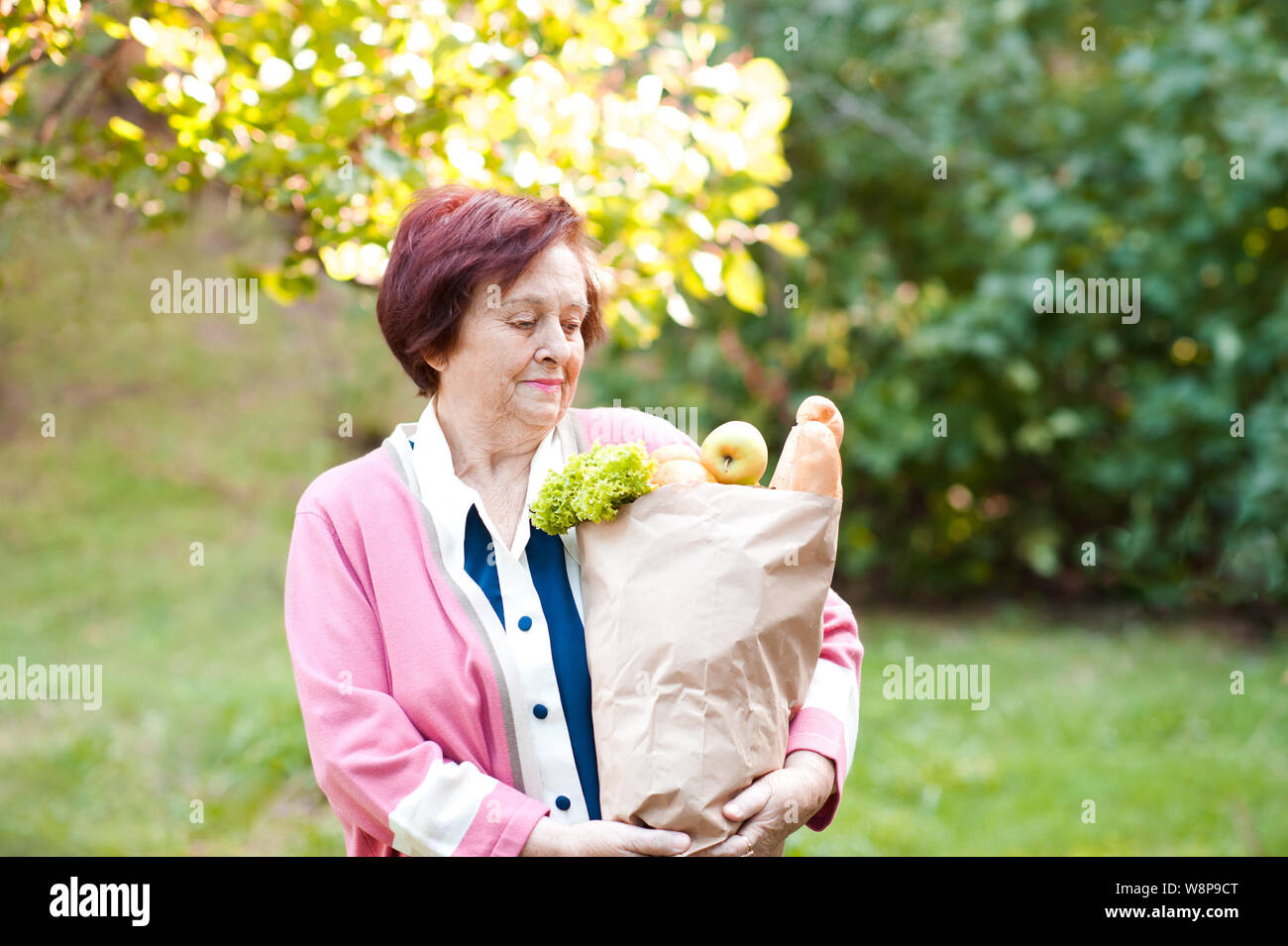 Smiling senior woman 70-75 year old holding paper food outdoors. 80s. Stock Photo