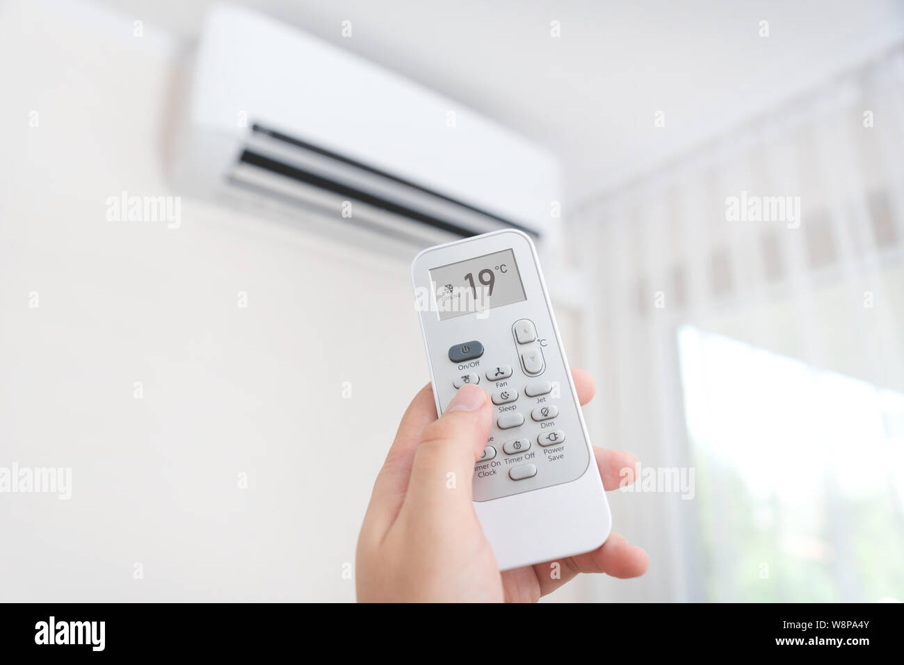 Hand with remote control directed on air conditioner. Home air conditioning concept Stock Photo