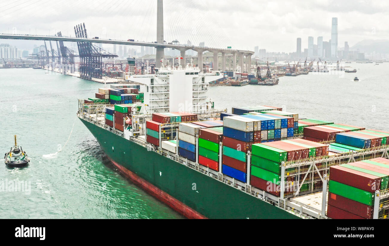 Large cargo ship transporting shipment container arriving Hong Kong port, bridge and city background drone aerial view. Freight transportation concept Stock Photo