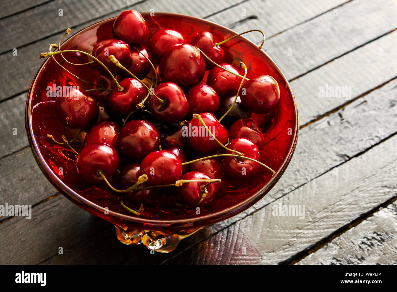 Fresh, ripe cherries in a red glass bowl on black wooden board table background . View from above with copy space Stock Photo