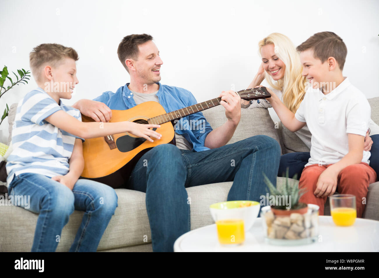 Happy caucasian family smiling, playing guitar and singing songs together at cosy modern home Stock Photo