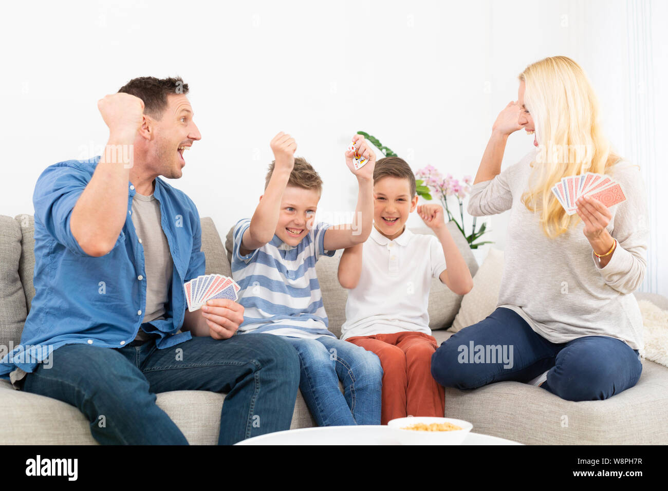 Happy family playing card game on living room sofa at home and having fun together celebrating the game winner Stock Photo