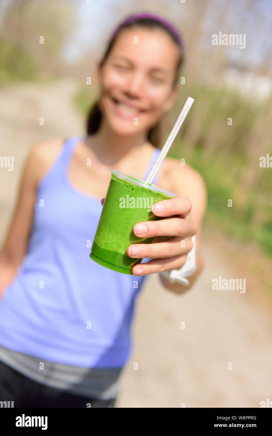 Green vegetable smoothie - healthy eating concept. Close up of green vegetable detox smoothie with spinach. Woman hand holding vegetable smoothies outdoors in forest. Stock Photo