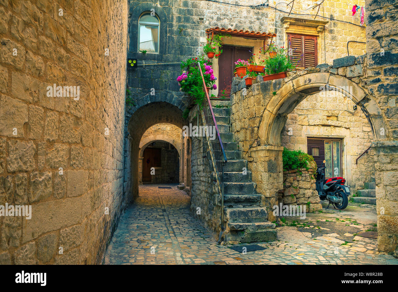 Picturesque narrow street with stone houses. Rustic stone houses and entrances decorated with flowers. Cozy street with antique houses and narrow alle Stock Photo