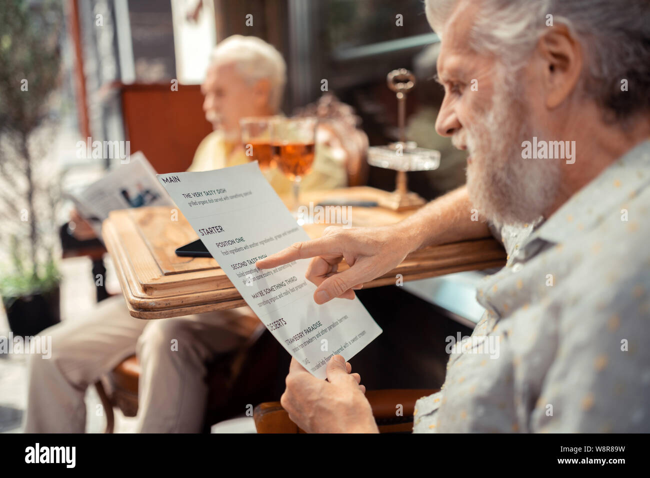 Close up of grey-haired bearded man holding menu and choosing dish Stock Photo