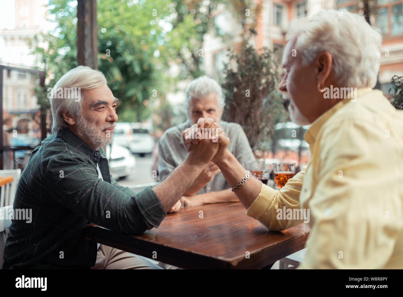 Men trying arm-wrestling while sitting outside pub Stock Photo