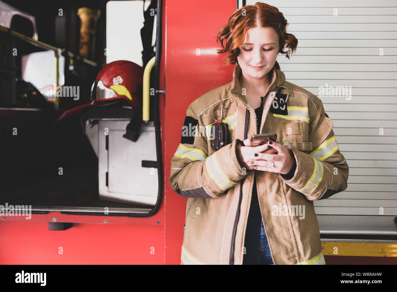 Photo of young woman firefighter with phone in her hands against background of fire engine Stock Photo