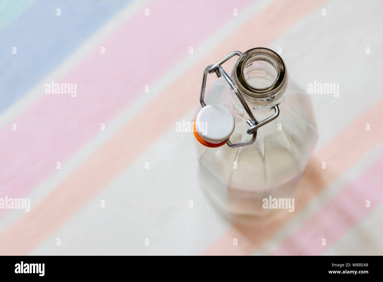 Top view of a glass bottle with a  wire bail clasp ceramic stopper on a blue, pink and orange stripped tablecloth Stock Photo