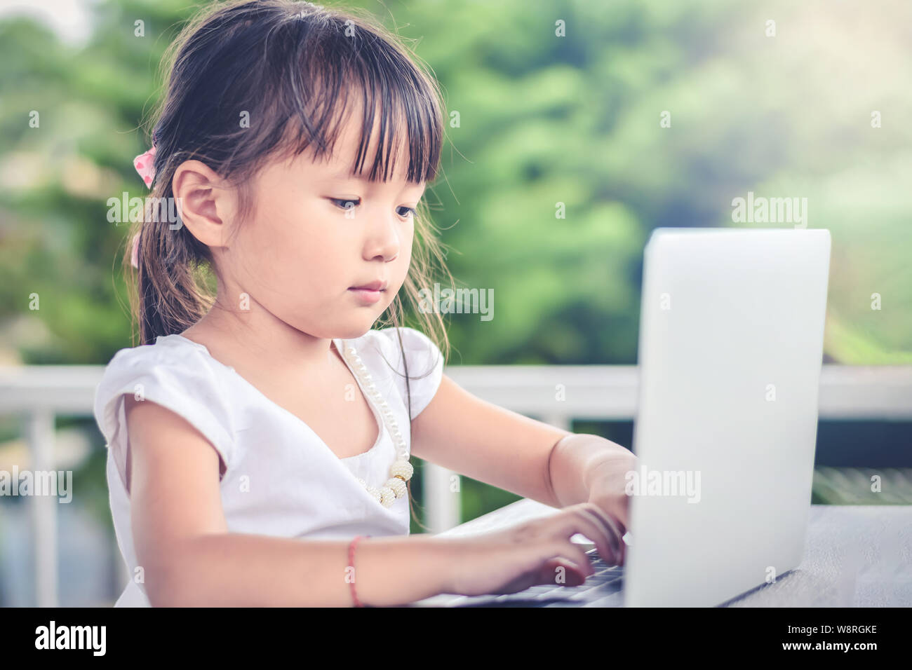 Asian little girl outdoors with smiley face using laptop in the garden