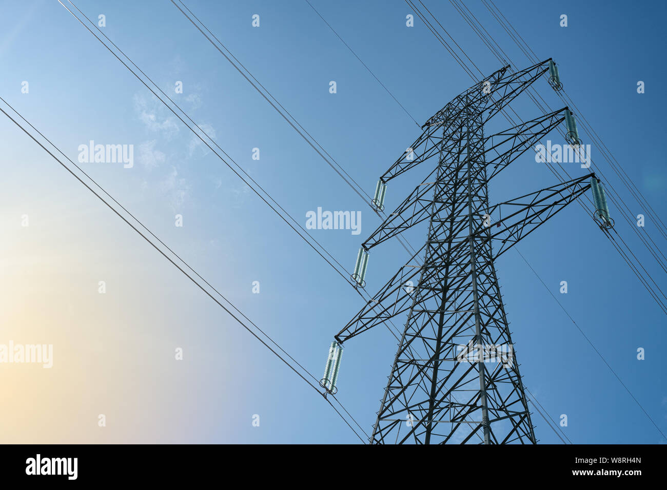Overhead electrical power lines on a transmission tower against blue sky background. Electric energy distribution concept. Stock Photo