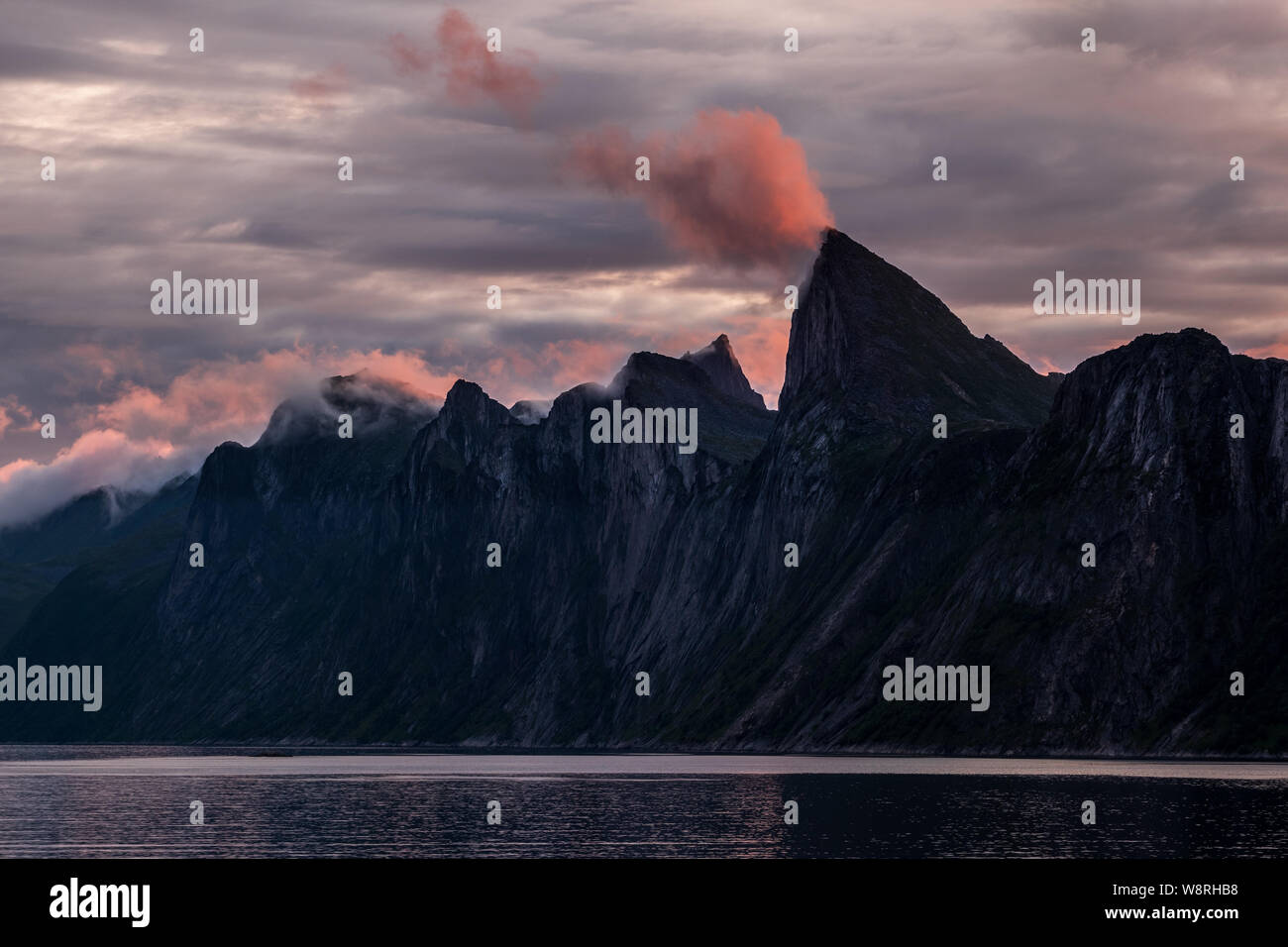 Impressive mountain range of Segla over a fjord at midnight under cloudy colorful sky, Senja, Norway Stock Photo