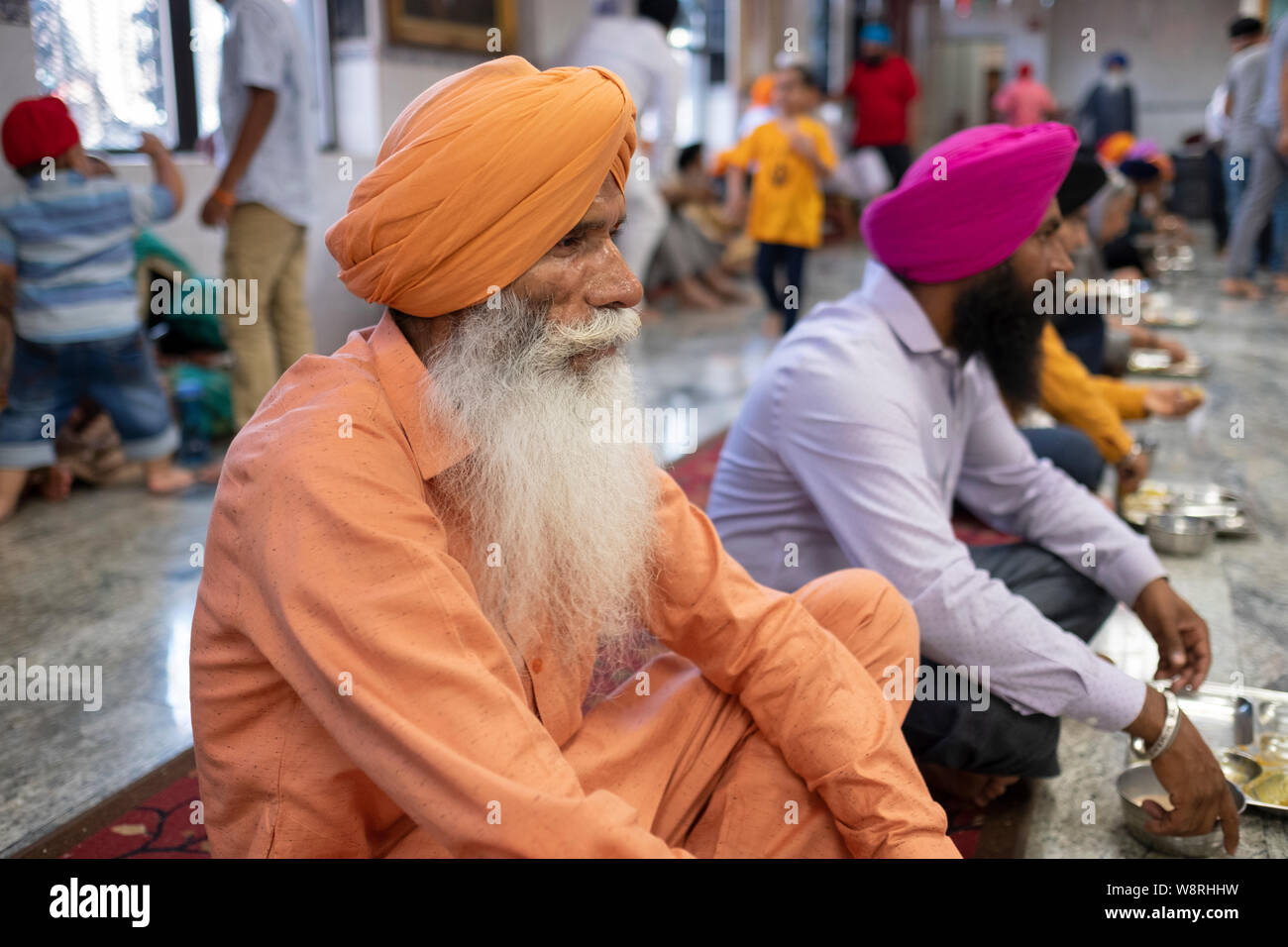 An older Sikh man dressed in orange who volunteers at a langar (communal dining hall) in a Sikh temple in South Ozone Park, Queens, New York City. Stock Photo