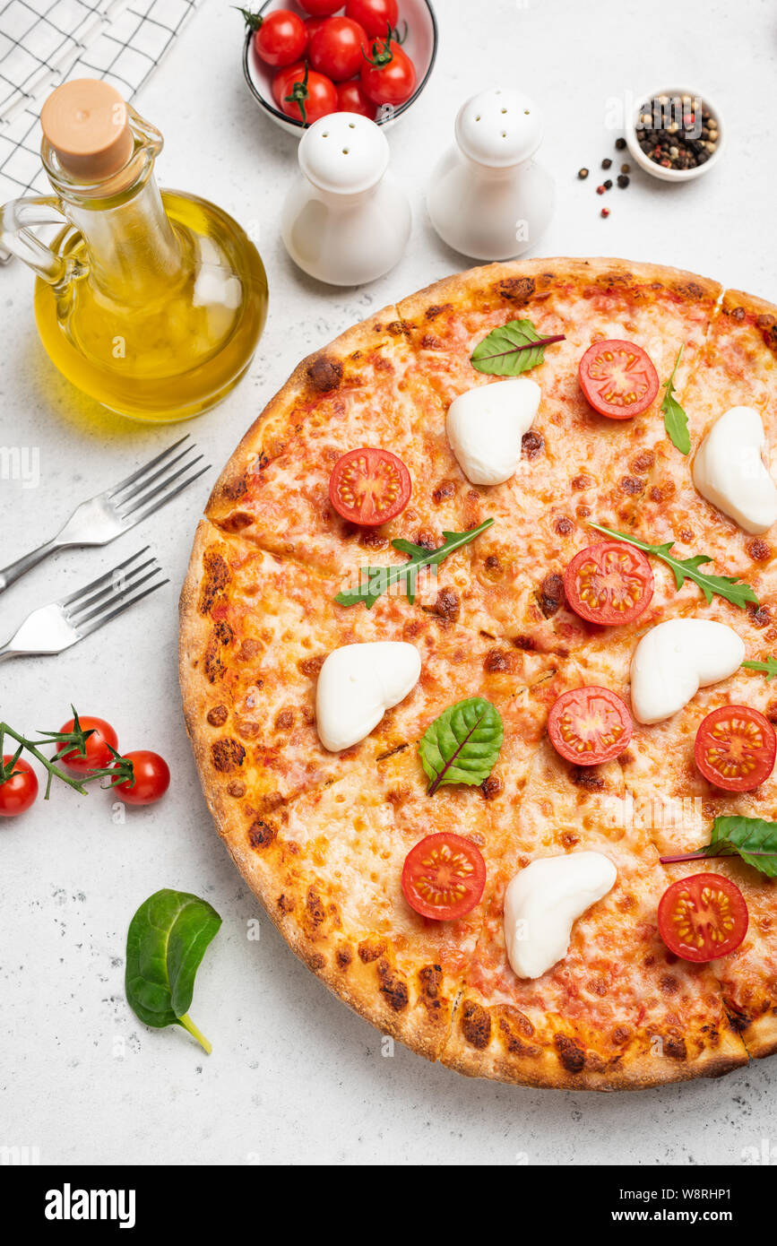Italian pizza with cheese, tomatoes, olive oil and green salad leaf on white background Stock Photo