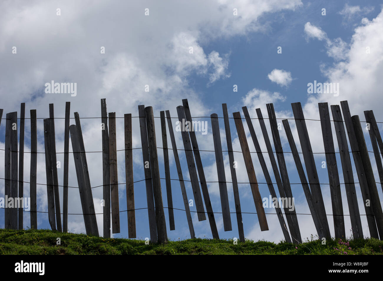 A wooden post and wire fence silhouetted against blue sky and clouds Stock Photo