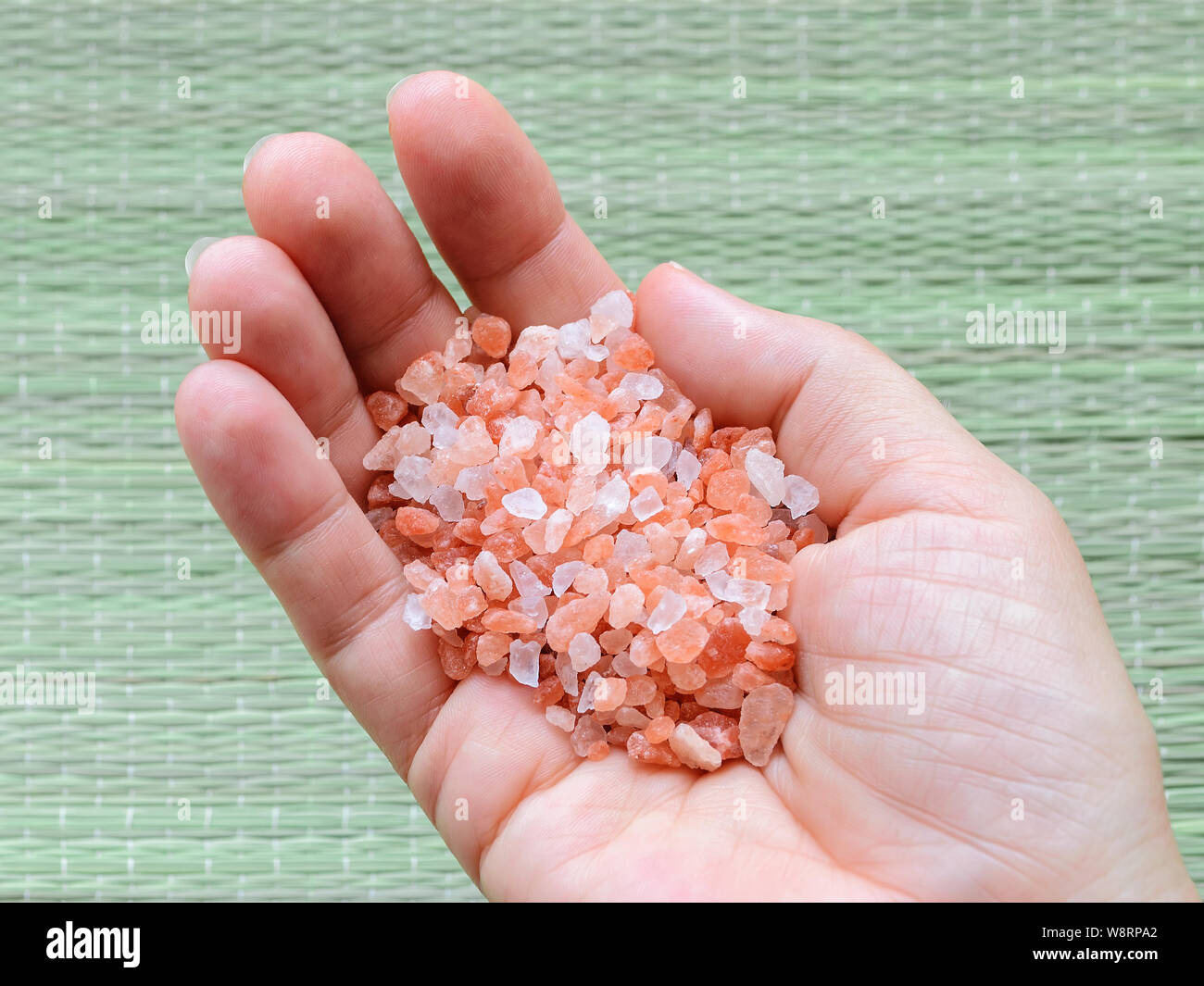Woman hand holding pink himalayan salt crystals over rough green mat. Himalayan salt is used in cooking, medicine and cosmetology. Top view. Stock Photo