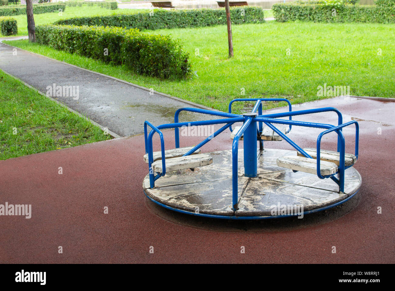 A small children's old carousel after the rain. Playground for children games old carousel for standing games. Blue knobs, white floor with peeling pa Stock Photo