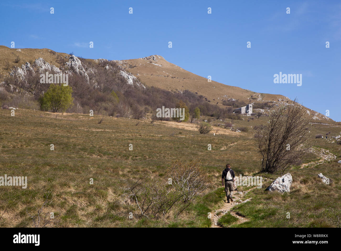 A man walking on a stony path on a meadow towards the little church on a hill Stock Photo