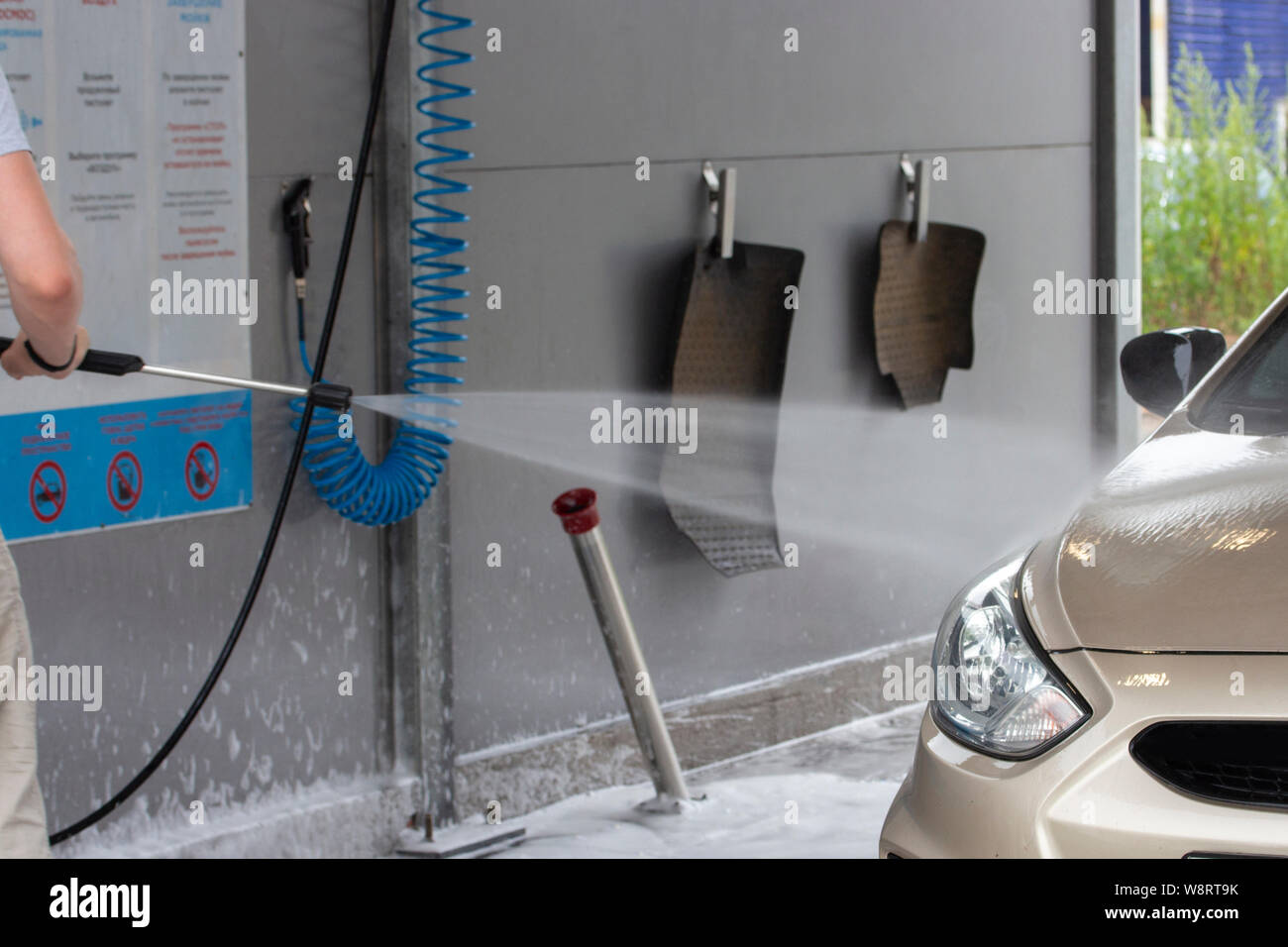 Car wash water jet is aimed at the car sedan, car mats hanging on clothespins, service cleaning Stock Photo