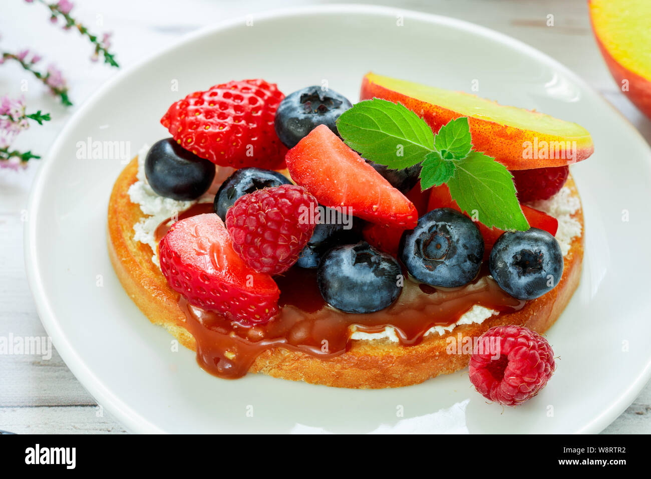 Delicious breakfast. Delicacy sandwich Toasts with cream cheese or mascarpone, caramel (iris toffee) and fresh berries - blueberries, raspberries, str Stock Photo
