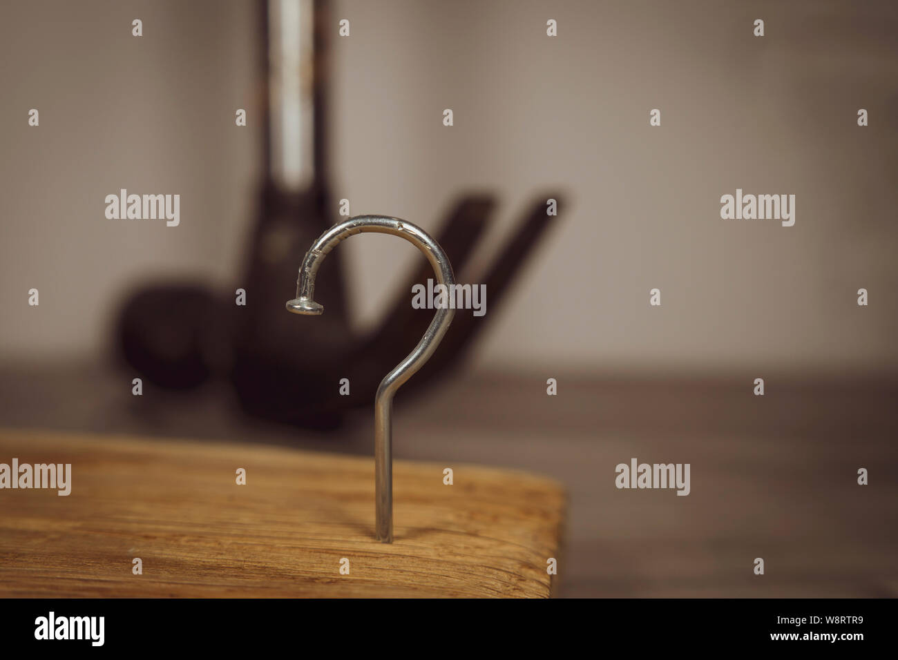 Construction nail shaped as question mark with blurred background of hammer, construction