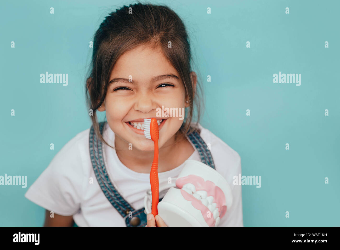Yes, my teeth is clean. Cute mixed raced girl brushing teeth at blue background. Stock Photo