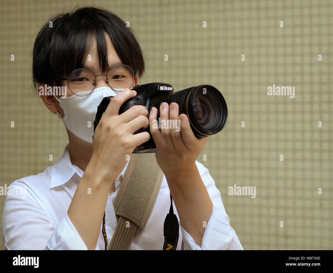Young Asian photographer with disposable face mask holds his Nikon D750 DSLR camera with both hands and poses for the camera. Stock Photo