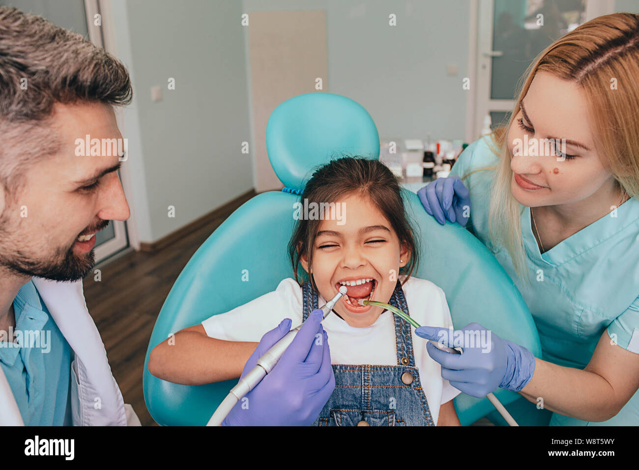 dentist and his assistant are treating the teeth of a little girl. Pediatric Dentistry Stock Photo