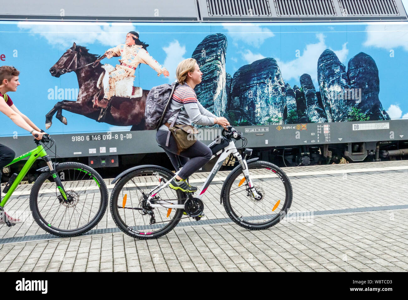 Germany Cyclists ride around the festival advertisement in Kurort Rathen. Winnetou on horseback and Bastei sandstone cliffs Germany Indians fest Stock Photo
