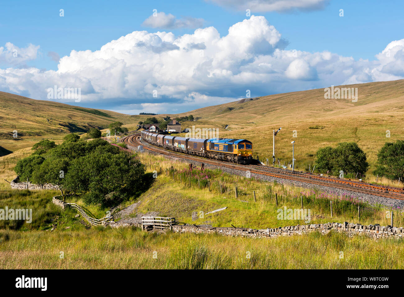 A Class 66 loco hauls a loaded stone train originating from Arcow Quarry out of rail sidings at Blea Moor on the Settle-Carlisle railway line. Stock Photo