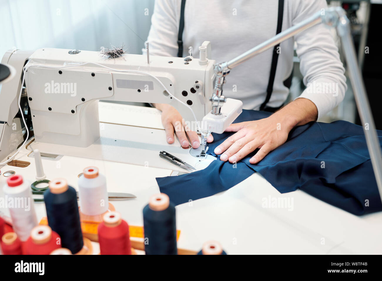 Hands of male tailor by sewing machine holding dark blue piece of textile Stock Photo