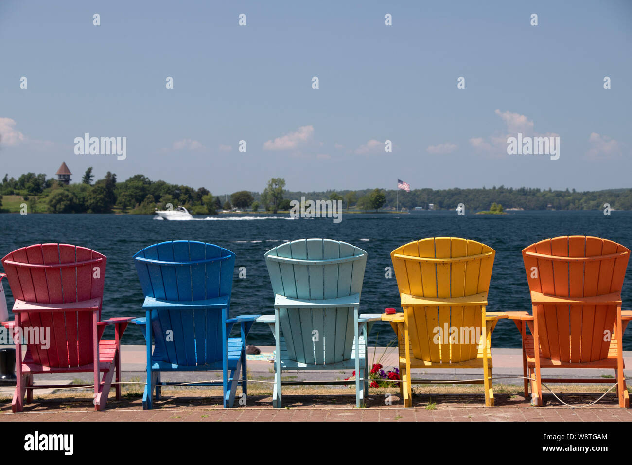 Colored Adirondack chairs in a row facing St Lawrence river during summer in town of Clayton, Jefferson County, NY, USA Stock Photo