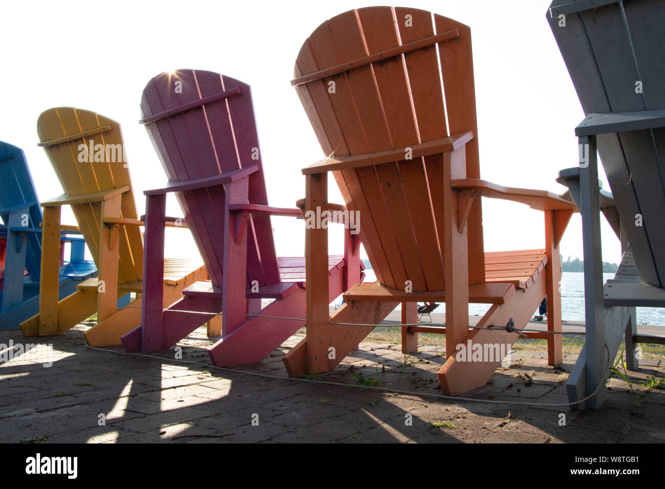 Side view of Adirondack chairs in a row with a sunburst in town of Clayton, NY, USA, St. Lawrence River, Jefferson County Stock Photo