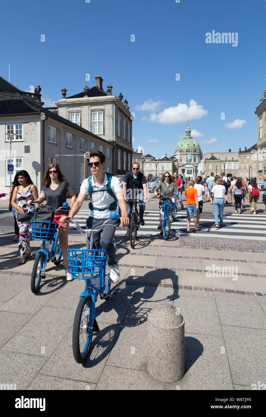Copenhagen bikes - people cycling bicycles in summer through Amalienborg Castle; Copenhagen city centre, Copenhagen Denmark Scandinavia Europe Stock Photo