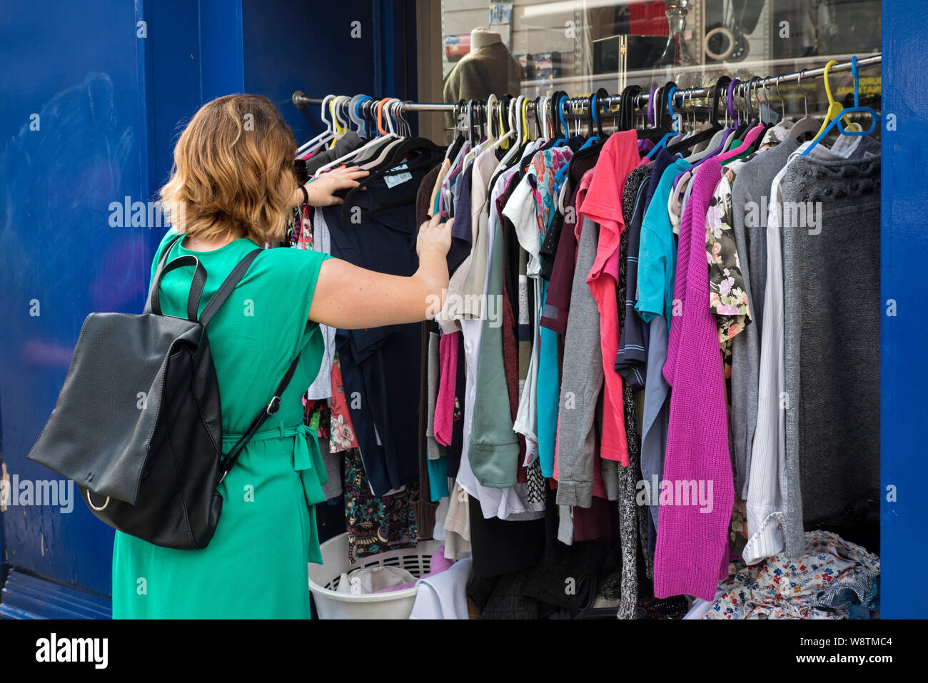 A young woman rummages through a rack of secondhand clothes outside a charity shop on Nicolson Street, Edinburgh, Scotland, UK. Stock Photo