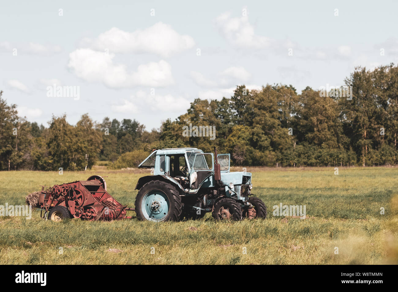 Old soviet tractor with assembly in the field. There is not anyone. There are clouds in the sky. Away the forest. Stock Photo