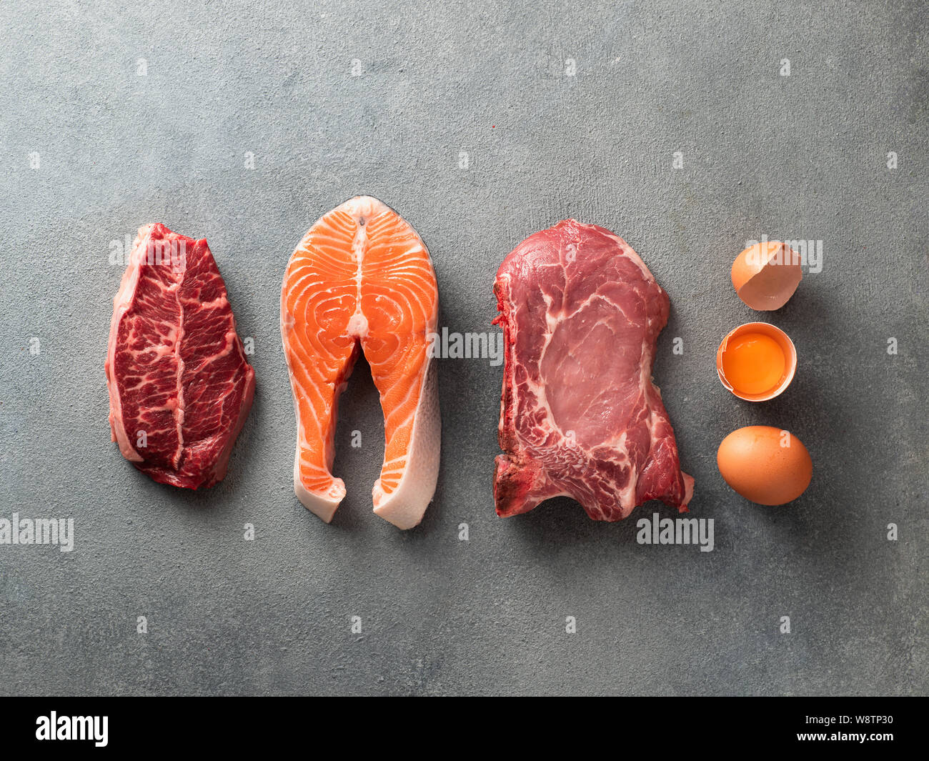 Carnivore or keto diet concept. Raw ingredients for zero carb or low carb diet - rib eye, salmon steak, pork, egg on gray stone background. Top view or flat lay. Stock Photo