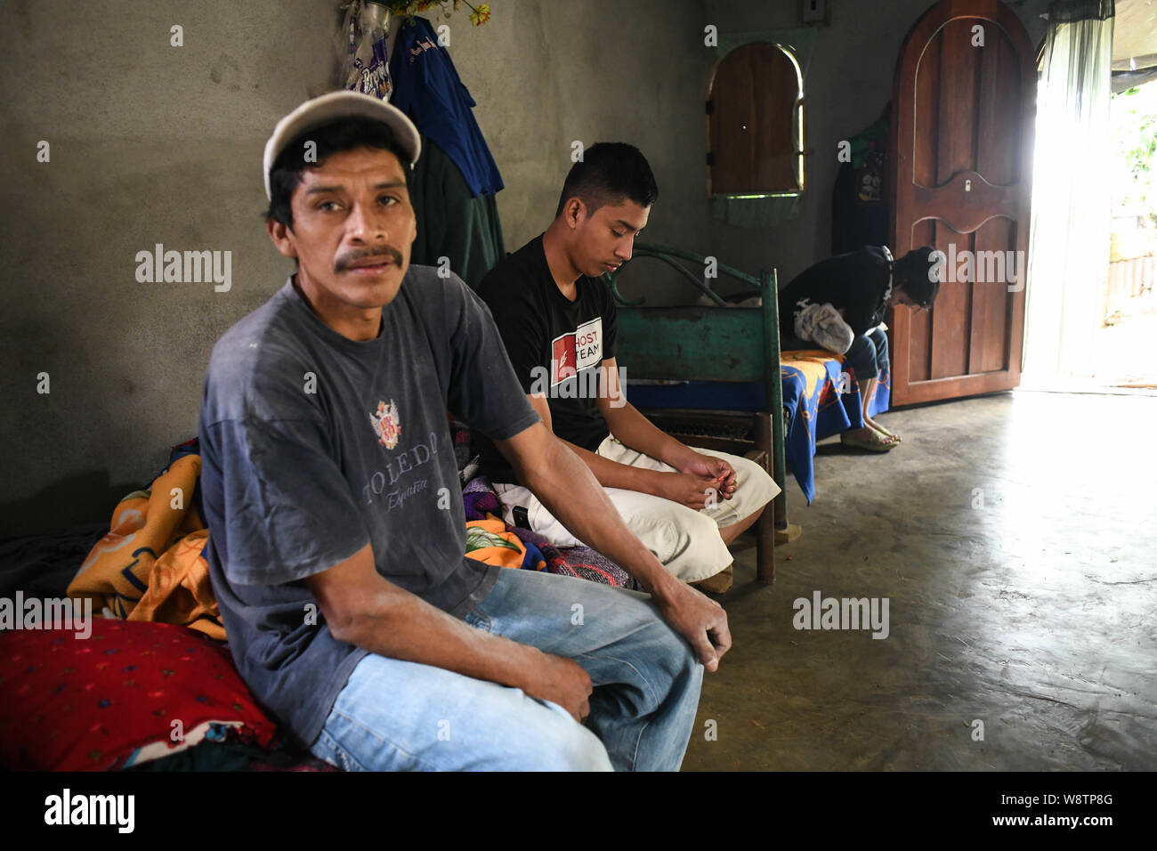 August 8, 2019, La Reforma, San Marcos, Guatemala: Lizardo Perez, 19, sits with his father, Edgar Perez, and sister Kelyn, in their one-room house in the neighborhood of Canton La Palma, in La Reforma, Guatemala. The parentsâ€” deep in debt from another sonâ€™s illness and now the smugglerâ€™s feeâ€” had pinned all their hopes on Lizardo making it to the U.S. Even as they now face losing their tiny house to creditors, they notice how Lizardo had finally escaped his permanent malnourishment during his 45 days in detention. â€œYou over took me Mâ€™ijo,â€ Edgar said.Â â€œLizardo is not even fitt Stock Photo