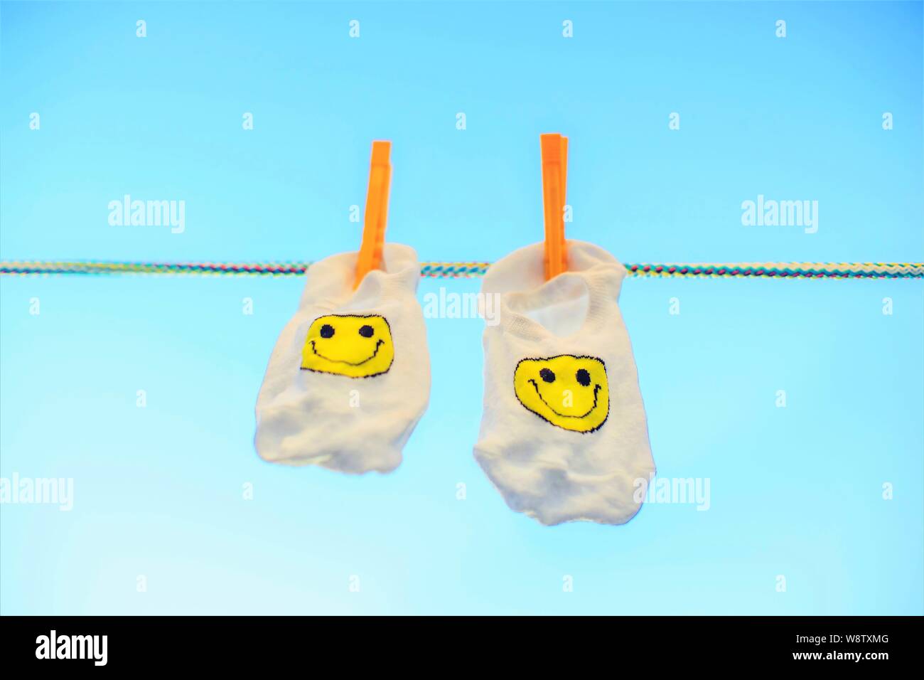 Two white socks with a yellow smiley emoticon hang on a rope with ...