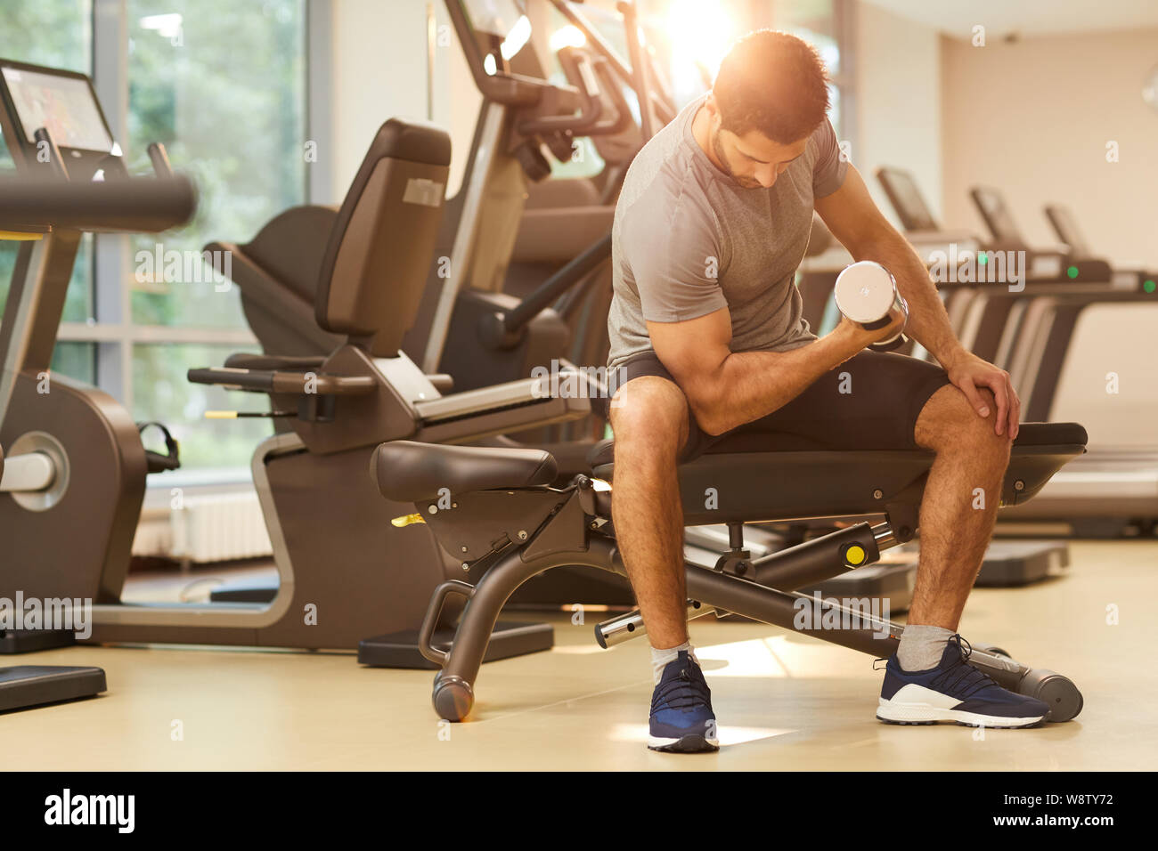 Full length portrait of muscular man lifting heavy dumbbells sitting on