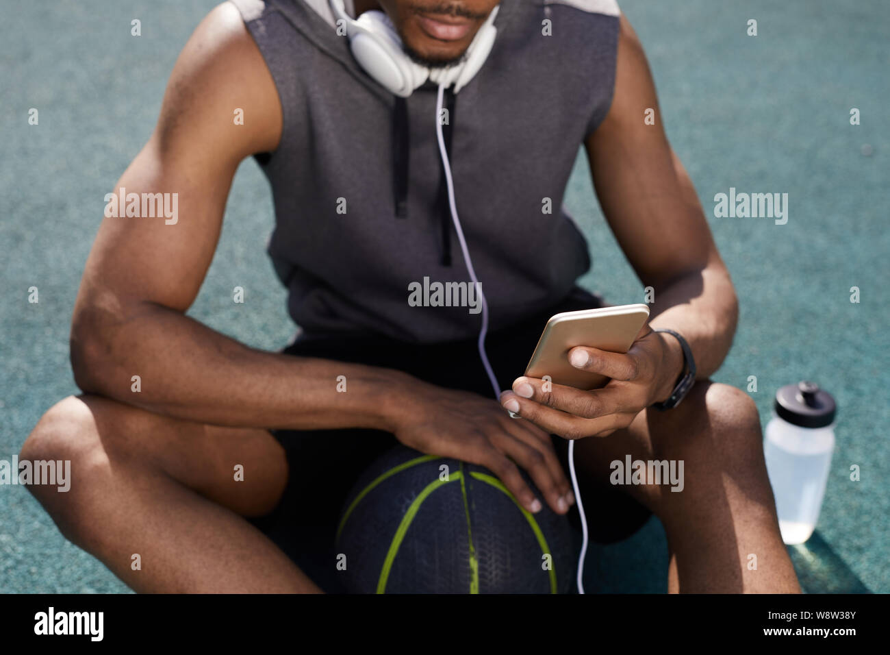 Mid-section background of contemporary African-American man using smartphone while sitting in basketball court, copy space Stock Photo