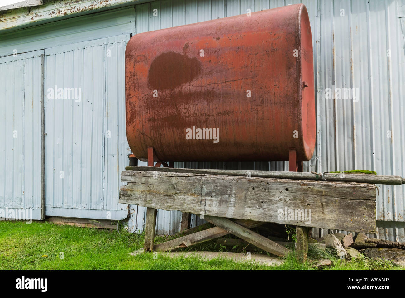 Red painted heating oil tank on old elevated wooden platform next to corrugated sheet metal cladded building in residential backyard Stock Photo