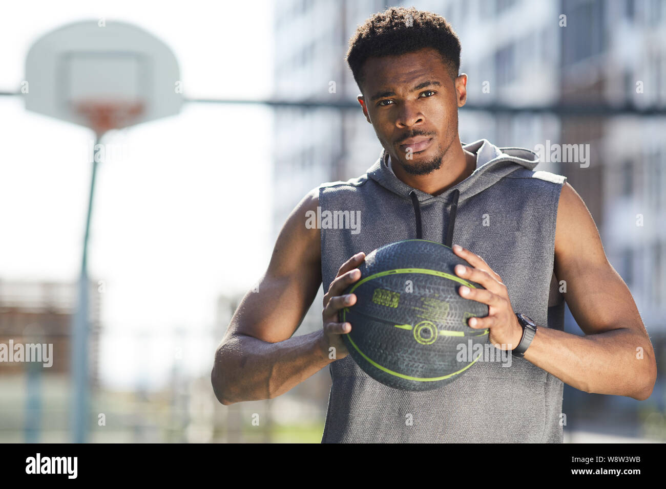 Waist up portrait of muscular African man holding basketball ball in outdoor court and looking at camera, copy space Stock Photo