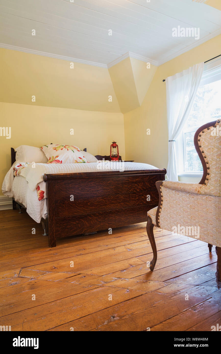 Antique double bed with wooden headboard and footboard, upholstered  armchair in guest bedroom with oil stained fir floorboards inside old 1900  house Stock Photo - Alamy