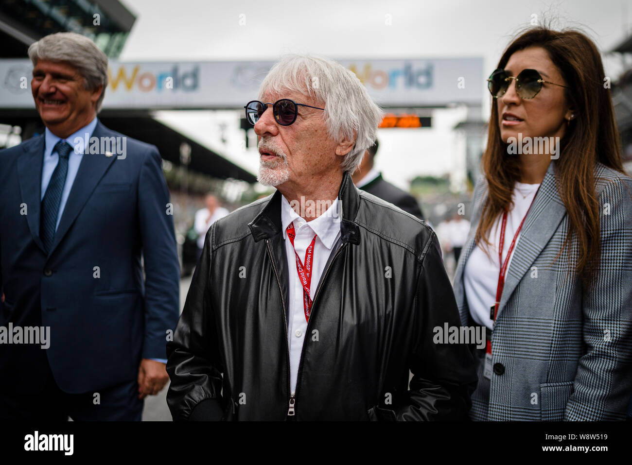 Bernie Ecclestone (C), Chairman Emeritus of the Formula One Group and his wife Fabiana Flosi (R) walk through the starting grid prior to the Austrian MotoGP Grand Prix race. Stock Photo