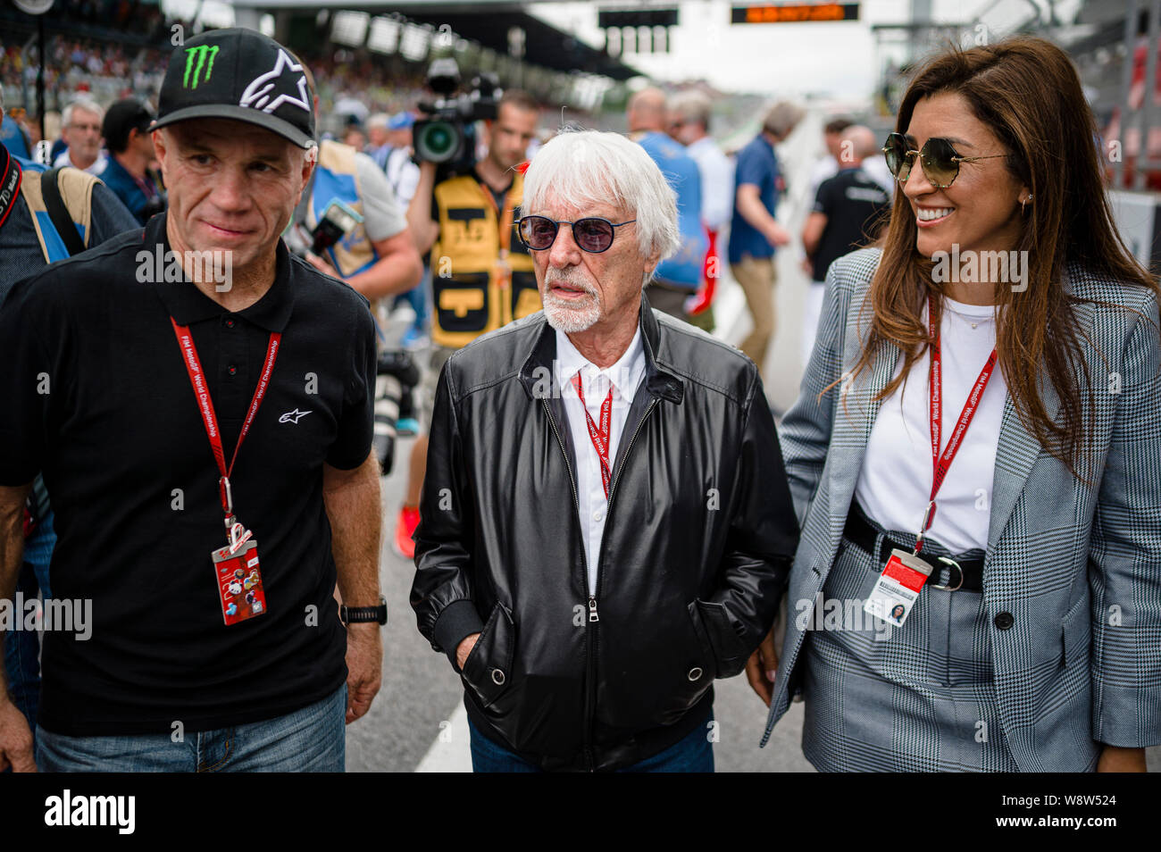 Randy Mamola (L), former American Grand Prix motorcycle racer, Bernie Ecclestone (C), Chairman Emeritus of the Formula One Group with his wife, Fabiana Flosi walk through the starting grid prior to the Austrian MotoGP Grand Prix race. Stock Photo