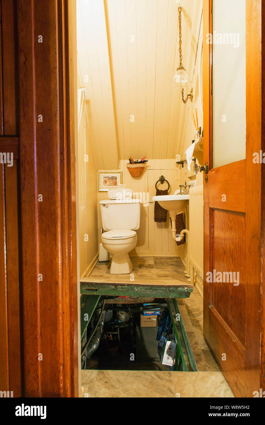 Water closet with white toilet and sink, plus opened trap door leading to basement laundry room inside an old 1927 American Four Squares house Stock Photo
